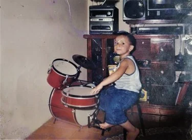 Tadeu ainda criança, sentado a uma bateria na sala de casa